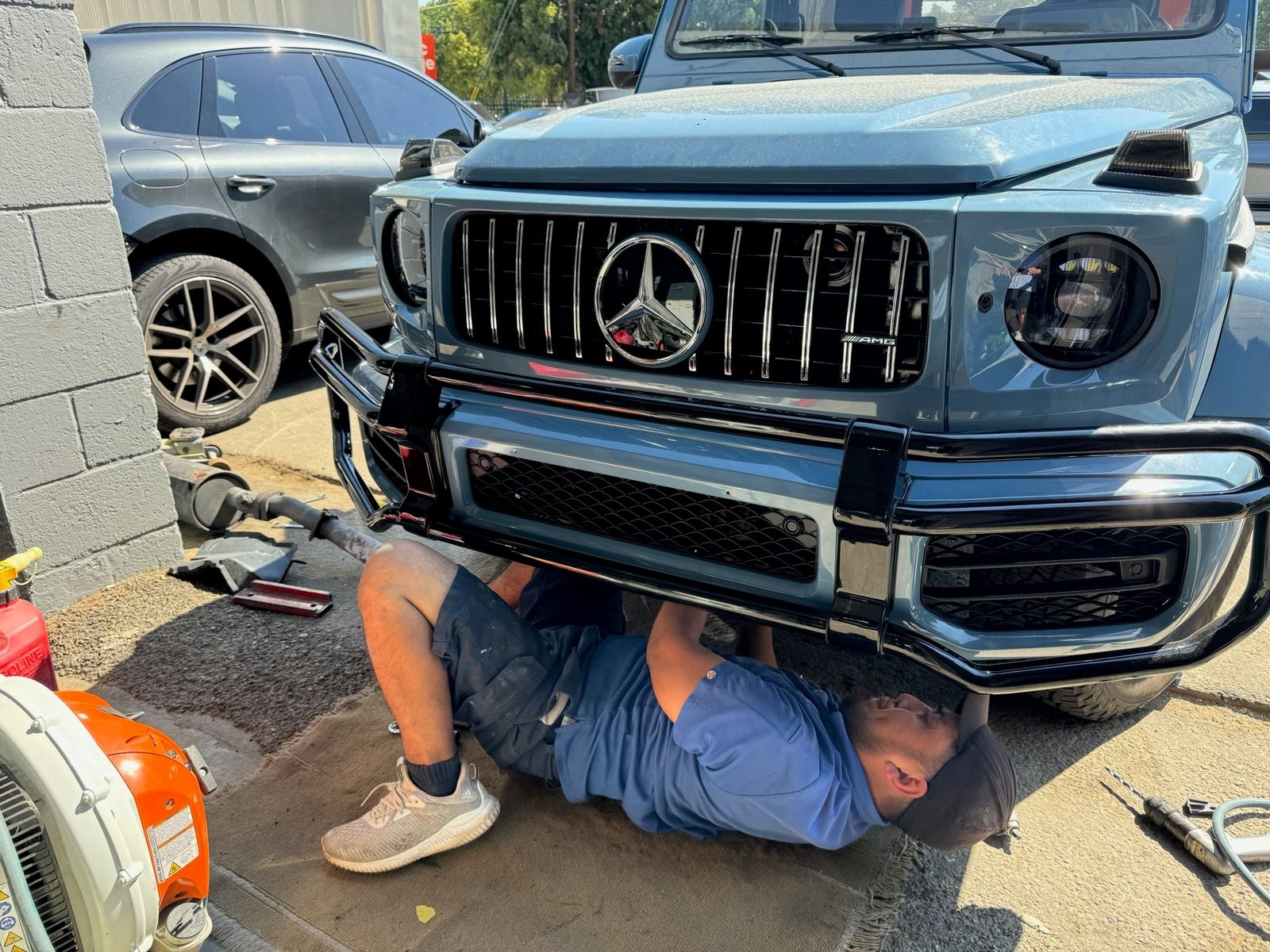 A technician working under the front bumper of a Mercedes G-Class at the shop