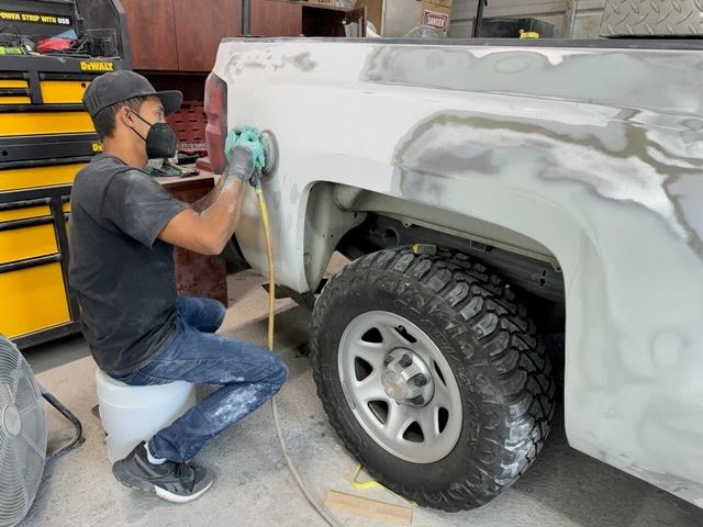 A technician block-sanding a truck bed in primer